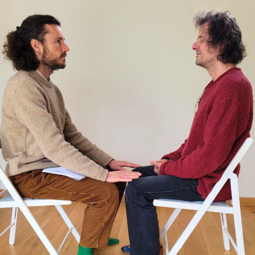 Deux hommes assis face à face, les mains jointes